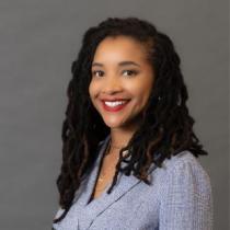 Headshot of Courtney Overton smiling in front of a grey background.