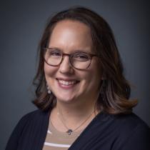 Woman with brown hair and wearing glasses smiles