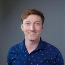 Headshot of Paul Mayo in front of a gray background. 