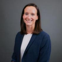 A woman with brown hair and wearing a blue blazer smiles