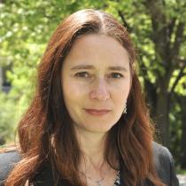 A woman with brown hair standing outside, looking at the camera. 