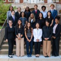 Group photo of BSOS DSAC standing on outdoor steps in front of a brick campus building, dressed in professional attire and smiling at the camera.