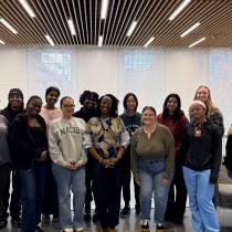 Group photo of HESP-GPS Puerto Rico cohort standing together indoors in a modern lounge or hallway with wood-slat ceiling lights and large windows, smiling at the camera.