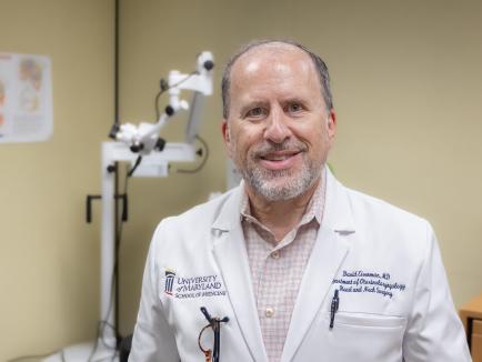 A man wears a labcoat while smiling at a camera