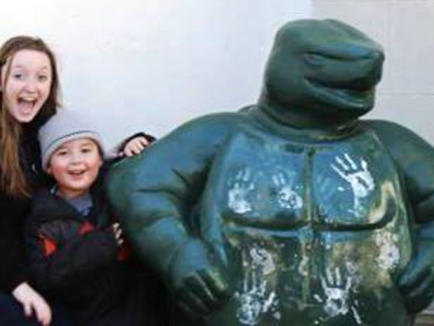 A smiling HESP student and LEAP student pose next to the Testudo statue, with the child leaning against the statue and both facing the camera.