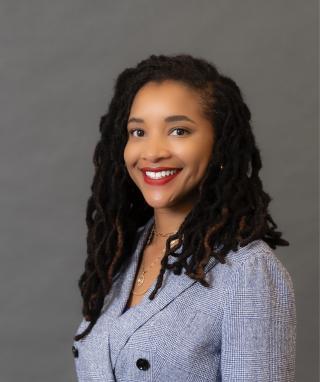Headshot of Courtney Overton smiling in front of a grey background.