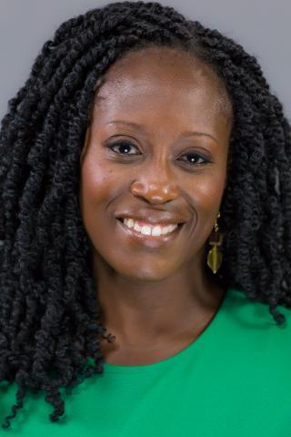 A headshot of Eliza Thompson wearing a bright green top and gold earrings against a neutral gray background.