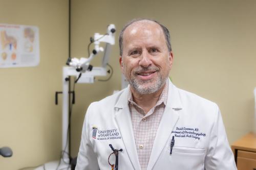 A man wears a labcoat while smiling at a camera