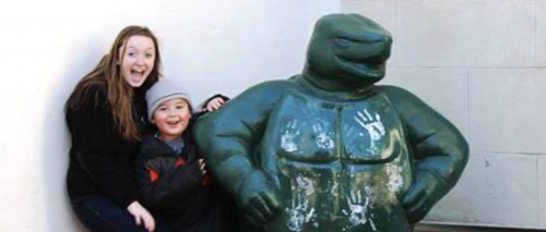 A smiling HESP student and LEAP student pose next to the Testudo statue, with the child leaning against the statue and both facing the camera.