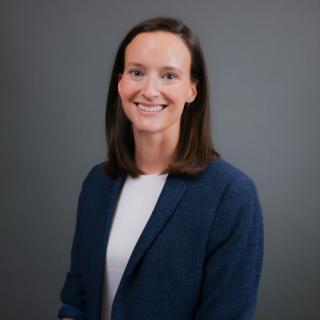 A woman with brown hair and wearing a blue blazer smiles