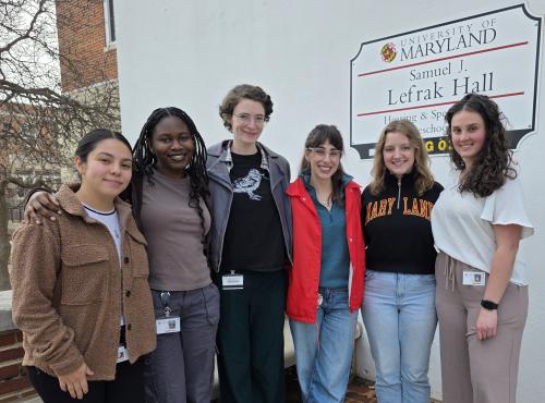 SIGNA coaches stand together outdoors beside a University of Maryland Samuel J. LeFrak Hall sign, smiling at the camera.