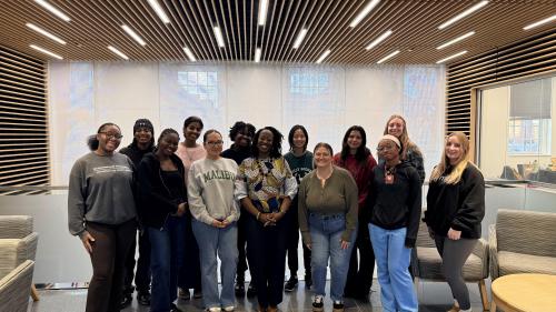 Group photo of HESP-GPS Puerto Rico cohort standing together indoors in a modern lounge or hallway with wood-slat ceiling lights and large windows, smiling at the camera.